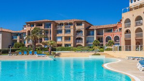 A hotel with a large swimming pool, multiple balconies, and a clear blue sky.