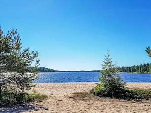 A beach with sand, a clear blue sky, and trees.