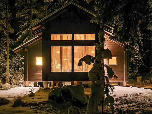 A cabin with large windows, a wooden exterior, and a snow-covered ground.