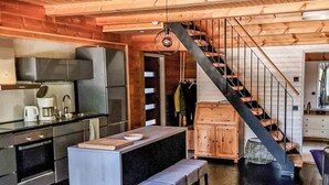 A modern kitchen with a central island, a staircase with a black railing, and wooden walls.