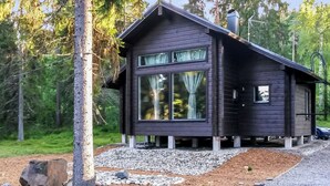 A modern cabin with large windows, a chimney, and is surrounded by a forest.