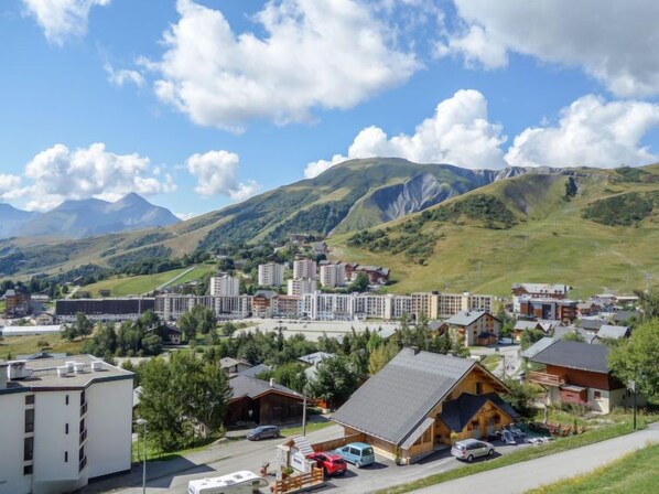 Un pueblo de montaña con una mezcla de edificios modernos y tradicionales, un área de estacionamiento y vistas de las colinas circundantes.