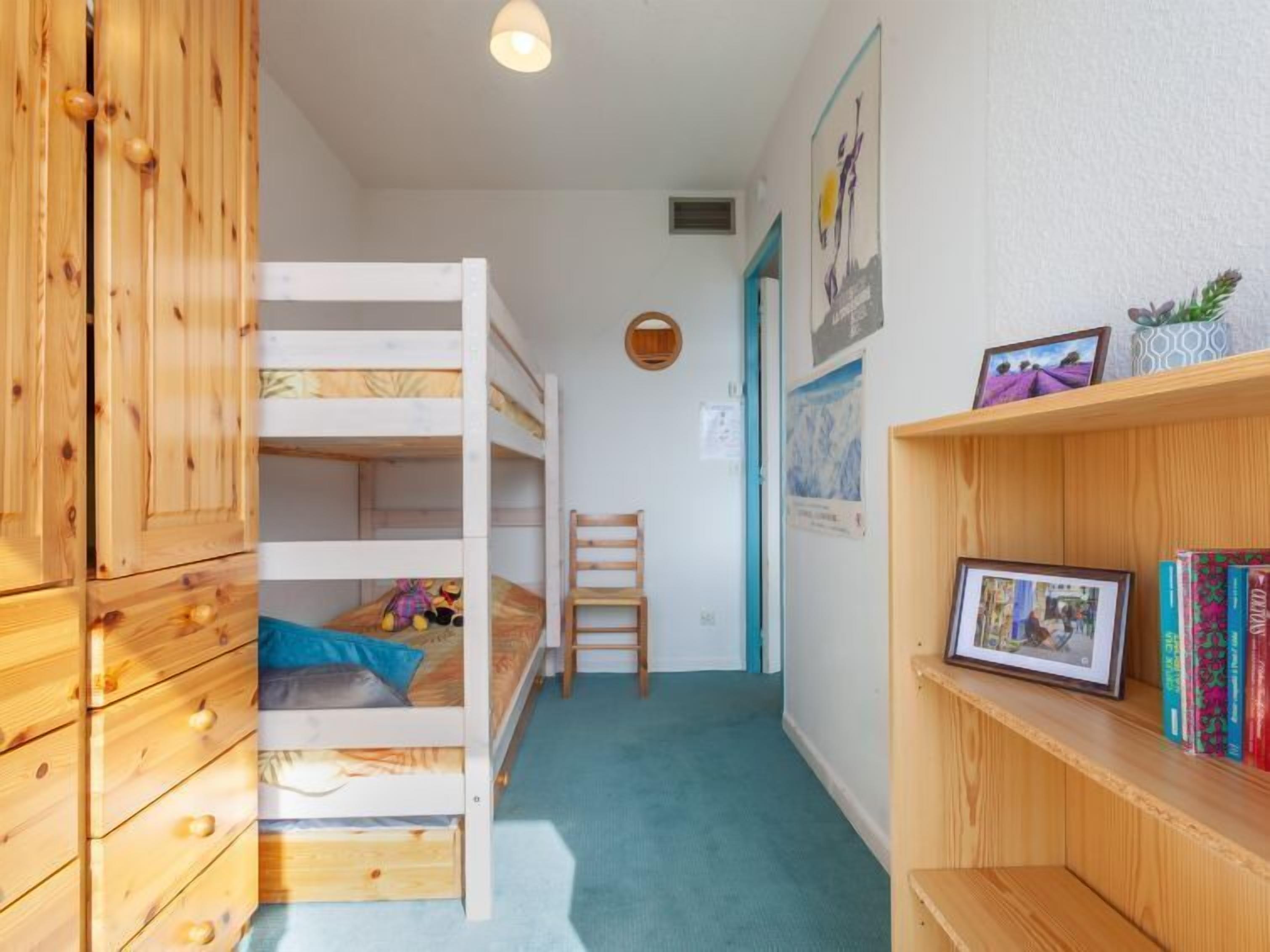 Una litera infantil con un armario de madera, una silla pequeña y una estantería llena de libros y una foto enmarcada.