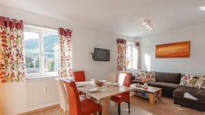 Ein modernes Wohnzimmer mit Essbereich, ausgestattet mit einer Couch, einem Fernseher und Blick ins Freie.