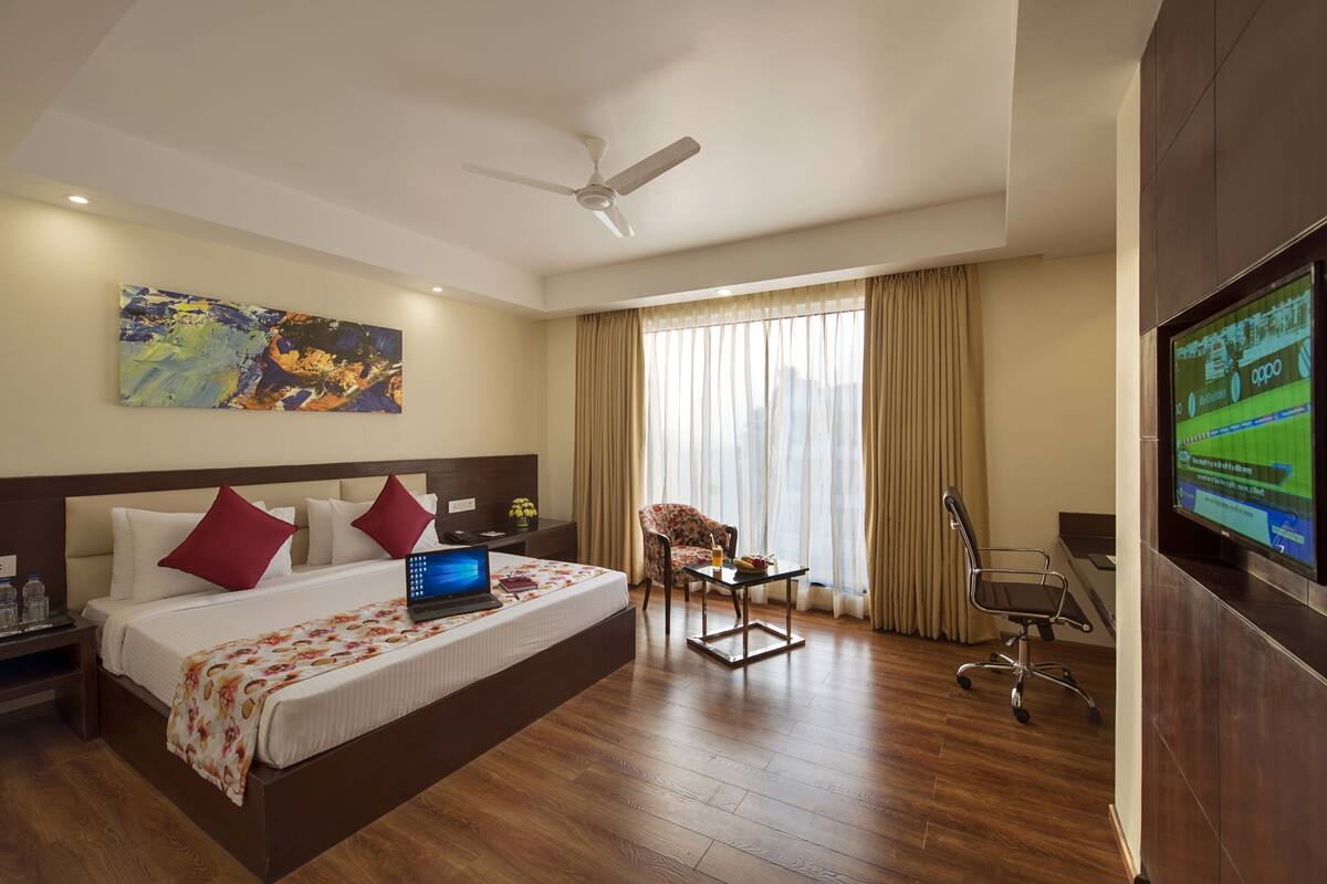 Una habitación de hotel con cama, escritorio, silla, televisor y ventilador de techo.