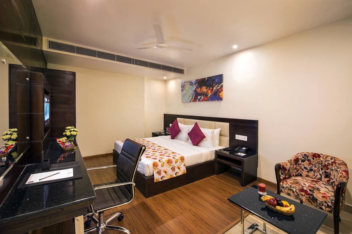 Habitación de hotel con cama, escritorio, silla y una mesita con fruta.