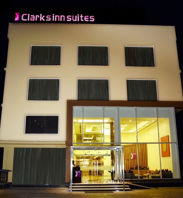 Entrada de un hotel con mostrador de recepción, una zona de estar en el interior y un cartel que dice "Clark's Inn Suites".