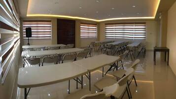 Une salle de conférence équipée de tables et de chaises, de grandes fenêtres avec stores et d’un plafond doté d’un éclairage encastré.