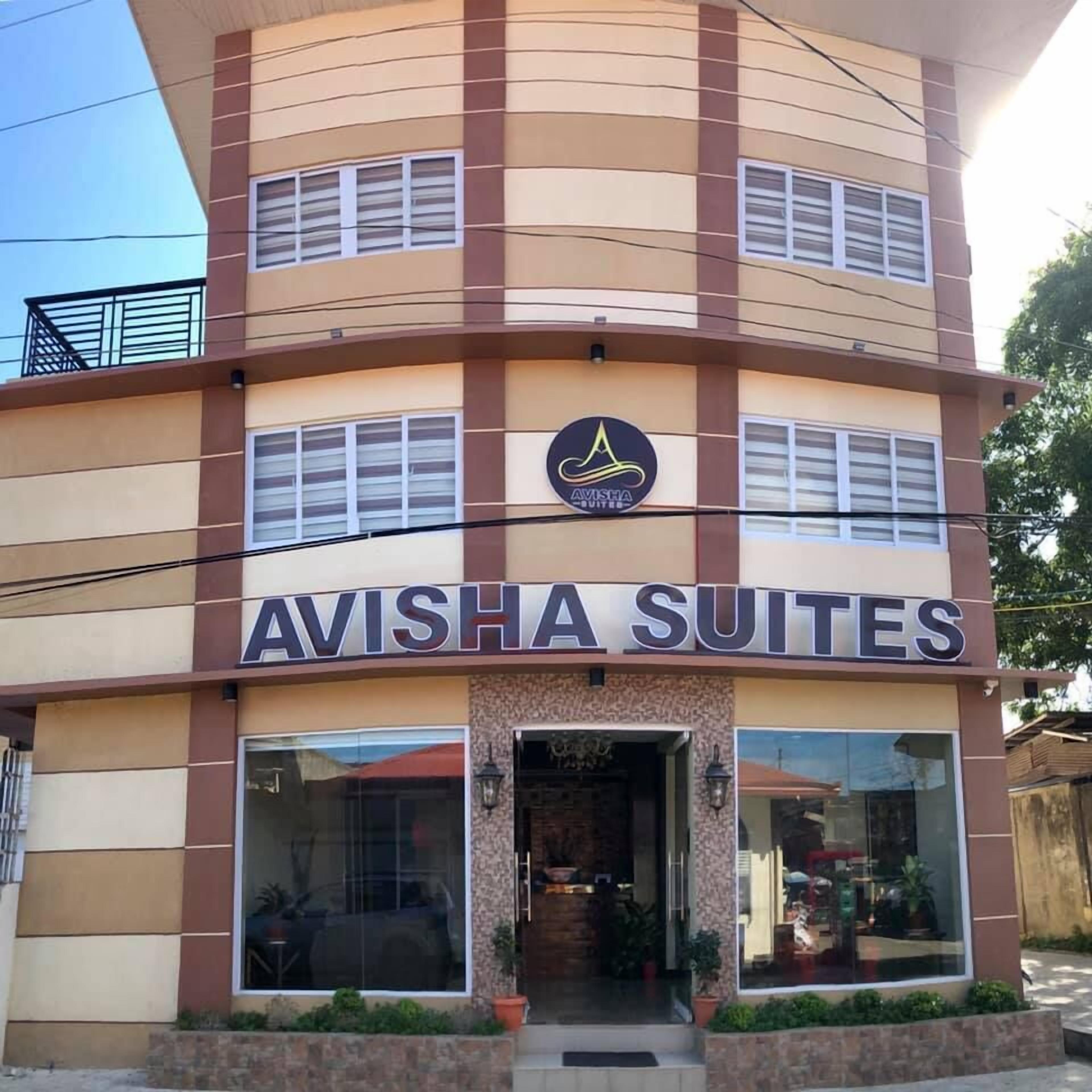 Un bâtiment portant l’enseigne « AVISHA SUITES », ce qui indique qu’il s’agit d’un hôtel ou d’un établissement proposant des hébergements.
