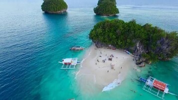 Vista aérea de una playa con aguas turquesas cristalinas, una orilla arenosa y varios barcos.
