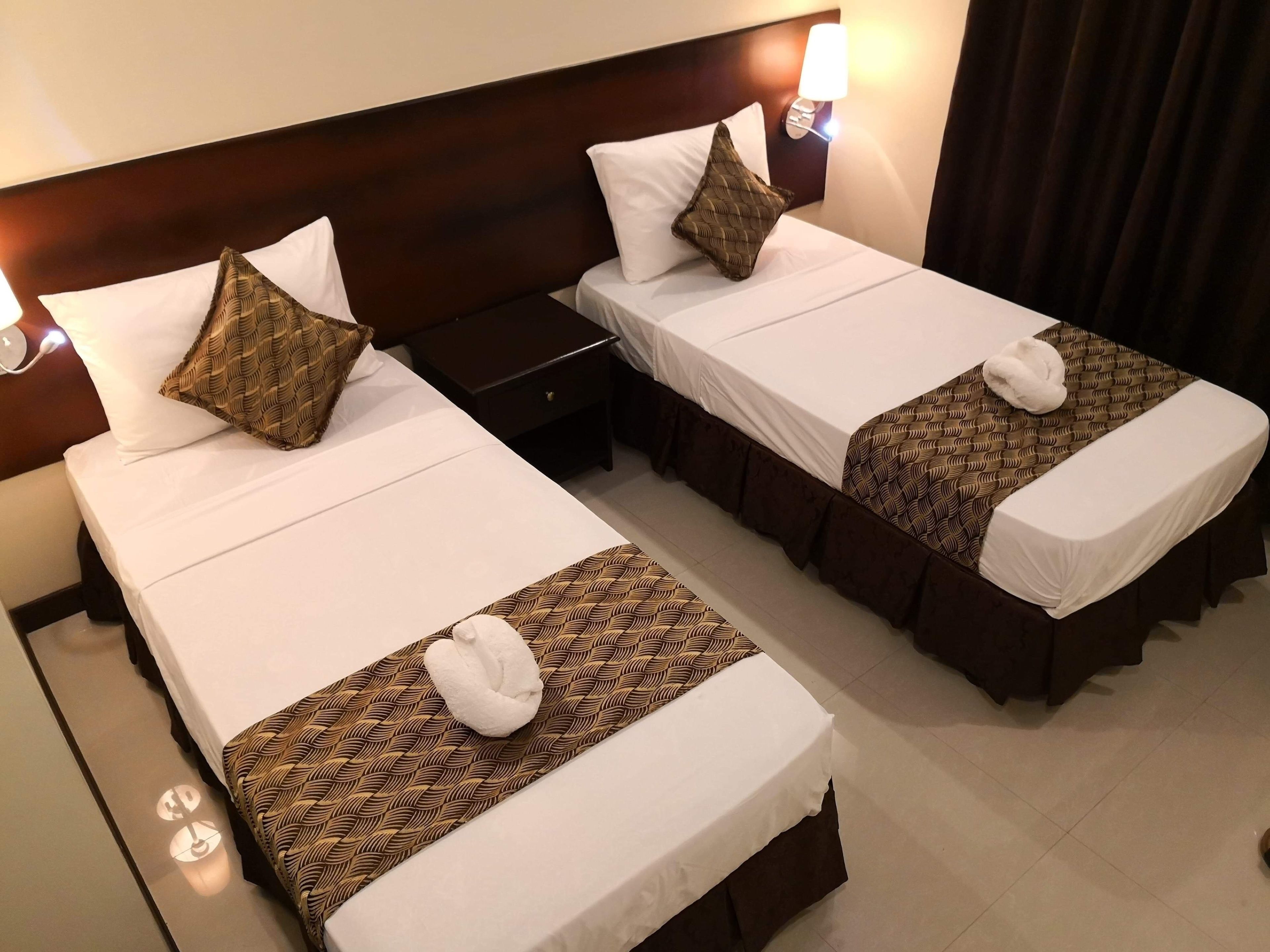 Due letti d'albergo con lenzuola bianche, runner da letto decorati e cuscini ornamentali.