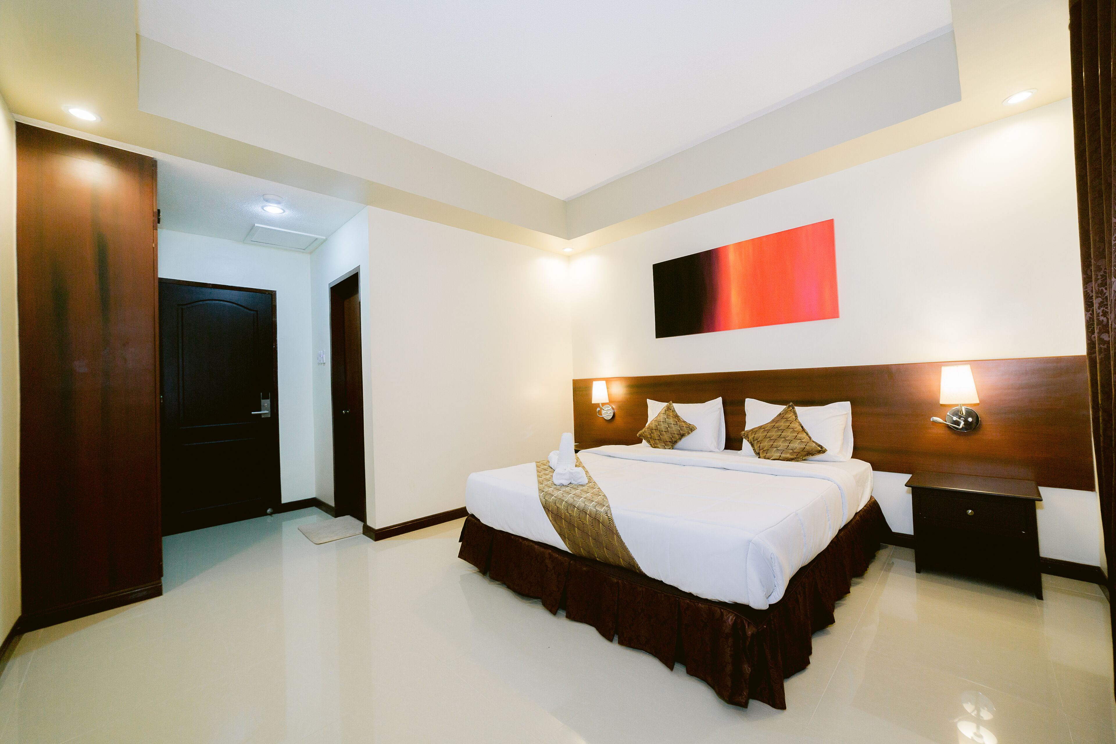 A hotel room with a large bed, a nightstand, a wall-mounted lamp, and a red abstract painting.