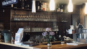 Una zona de bar con estanterías llenas de vasos y botellas, un letrero que dice "Wollbacher tor straBe" y un jarrón con flores en la barra.