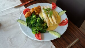 Un plato de comida con verduras y un trozo de carne, sobre una mesa con servilleta y cuchillo.