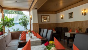 Un restaurante con una larga mesa dispuesta para comer, asientos acolchados y detalles decorativos como flores y servilletas.