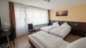 Habitación de hotel con dos camas, un escritorio con un ventilador, una silla y una ventana con cortinas.