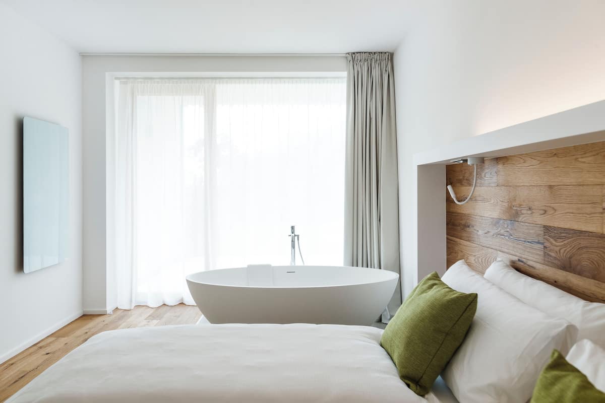 A modern bedroom with a large bed, a freestanding bathtub, and a wooden headboard.