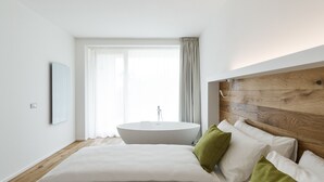 A modern bedroom with a large bed, a round bathtub, and a wooden headboard. - Alea Garda Lake Suite (Arco)