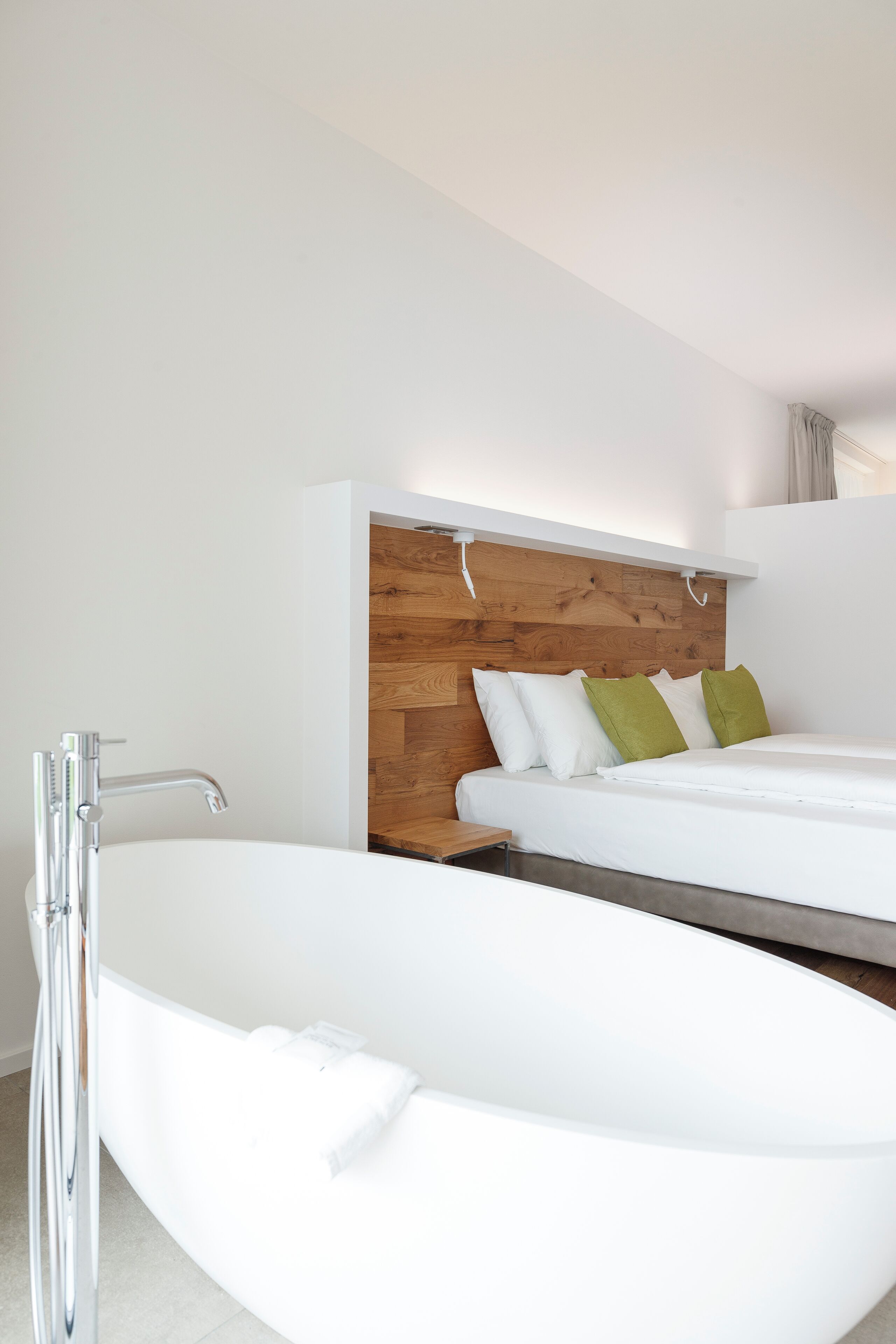 Een moderne badkamer met een vrijstaand bad, een houten hoofdeinde en een wit bed met groene kussens.