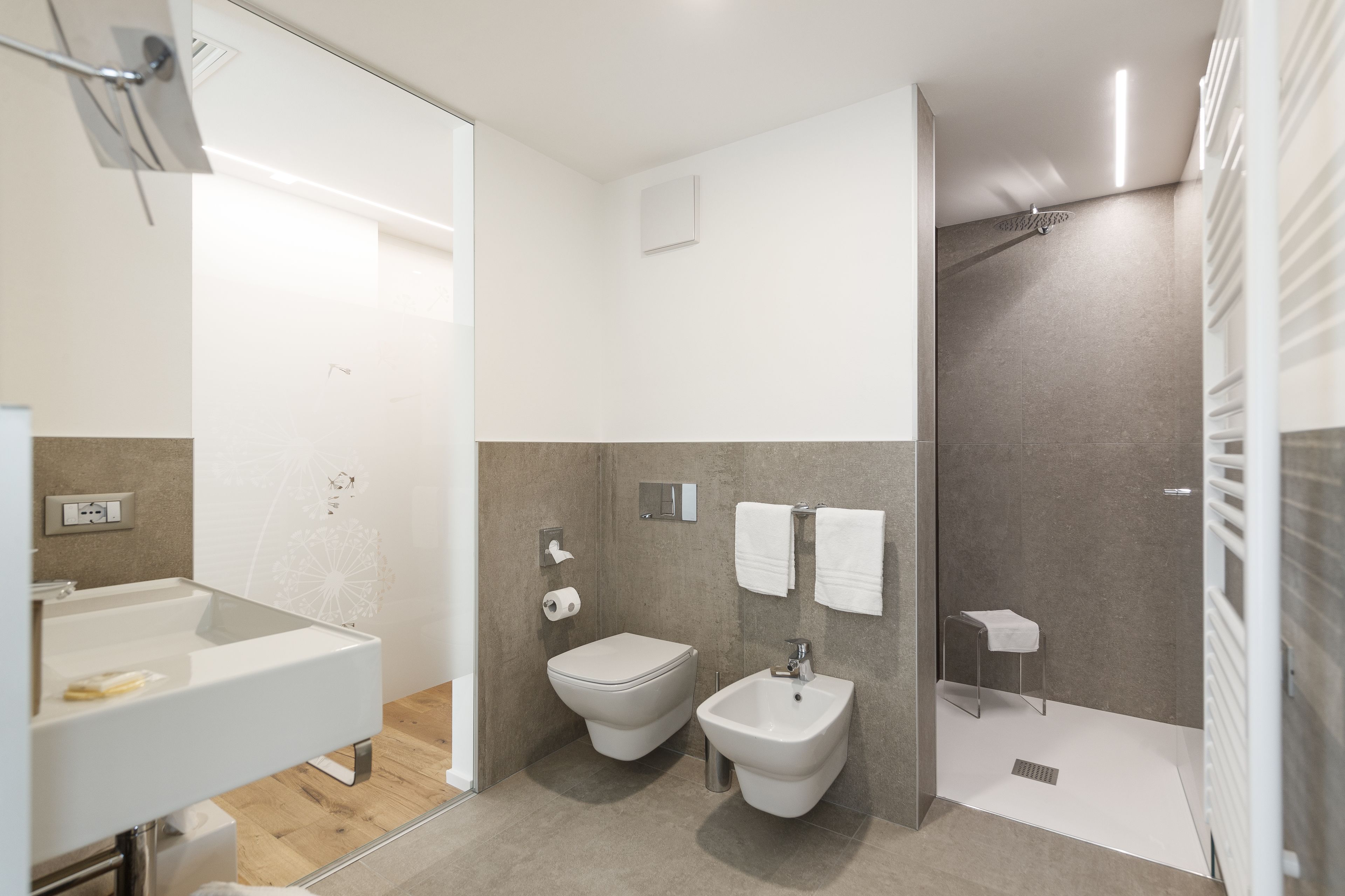Un bagno moderno con box doccia in vetro, un water, un bidet e un lavandino.