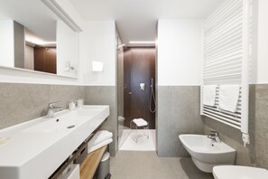 Un baño moderno con un lavamanos grande de color blanco, un bidé y una ducha con mampara de vidrio.
