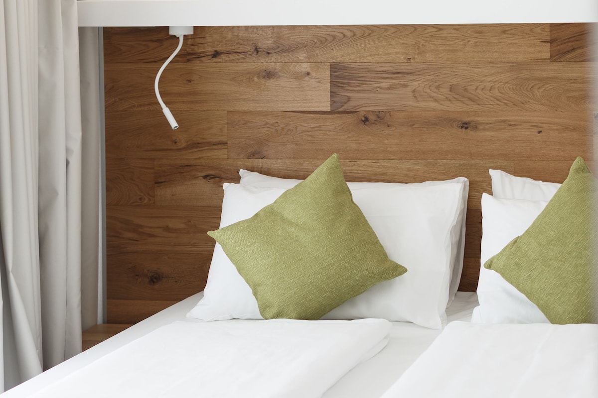 A neatly made bed with white bedding and green pillows, a wooden headboard, and a white wall.