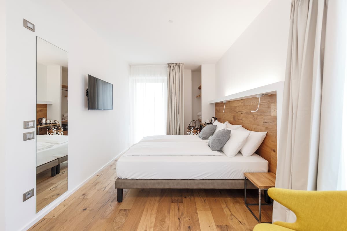 A modern bedroom with a large bed, a bedside table, a mirror, and a TV mounted on the wall.