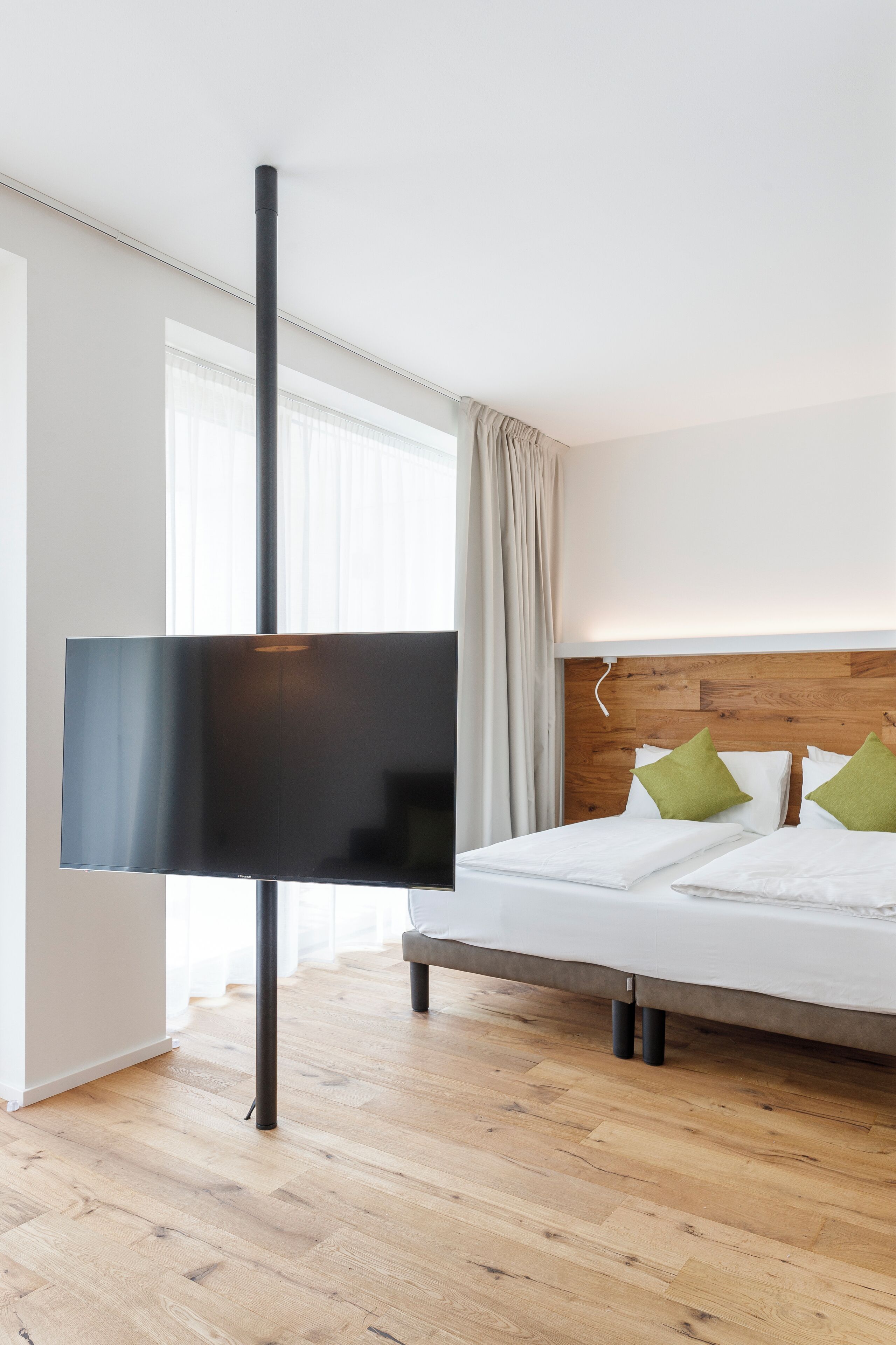 Une chambre d’hôtel moderne avec un grand lit, une tête de lit en bois et un téléviseur à écran plat fixé sur un support.