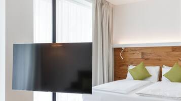 Une chambre d’hôtel moderne avec un grand lit, une tête de lit en bois et un téléviseur à écran plat fixé sur un support.