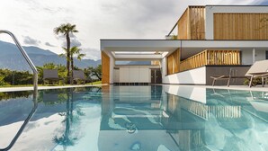 A modern pool area with clear water, lounge chairs, and a view of mountains. - Alea Garda Lake Suite (Arco)