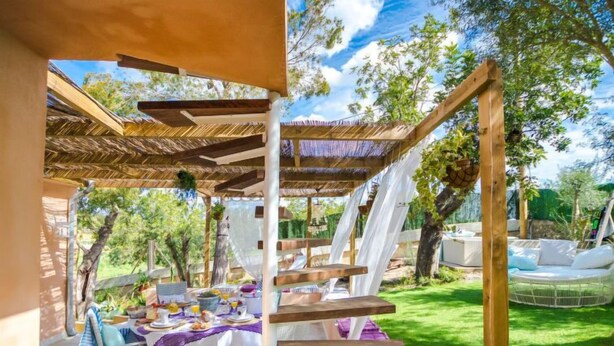 Un'area pranzo all'aperto coperta, con un tavolo apparecchiato per un pasto, circondata da un gazebo in legno e un prato.