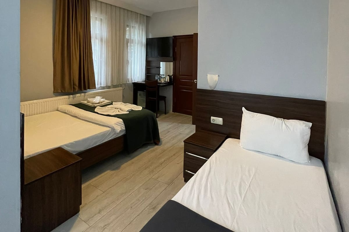 A hotel room with two beds, a desk, a chair, and a small kitchenette.