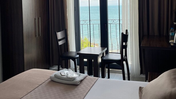 Ein Hotelzimmer mit Bett, Schreibtisch, zwei Stühlen, einem Kleiderschrank und einem großen Fenster mit Meerblick.