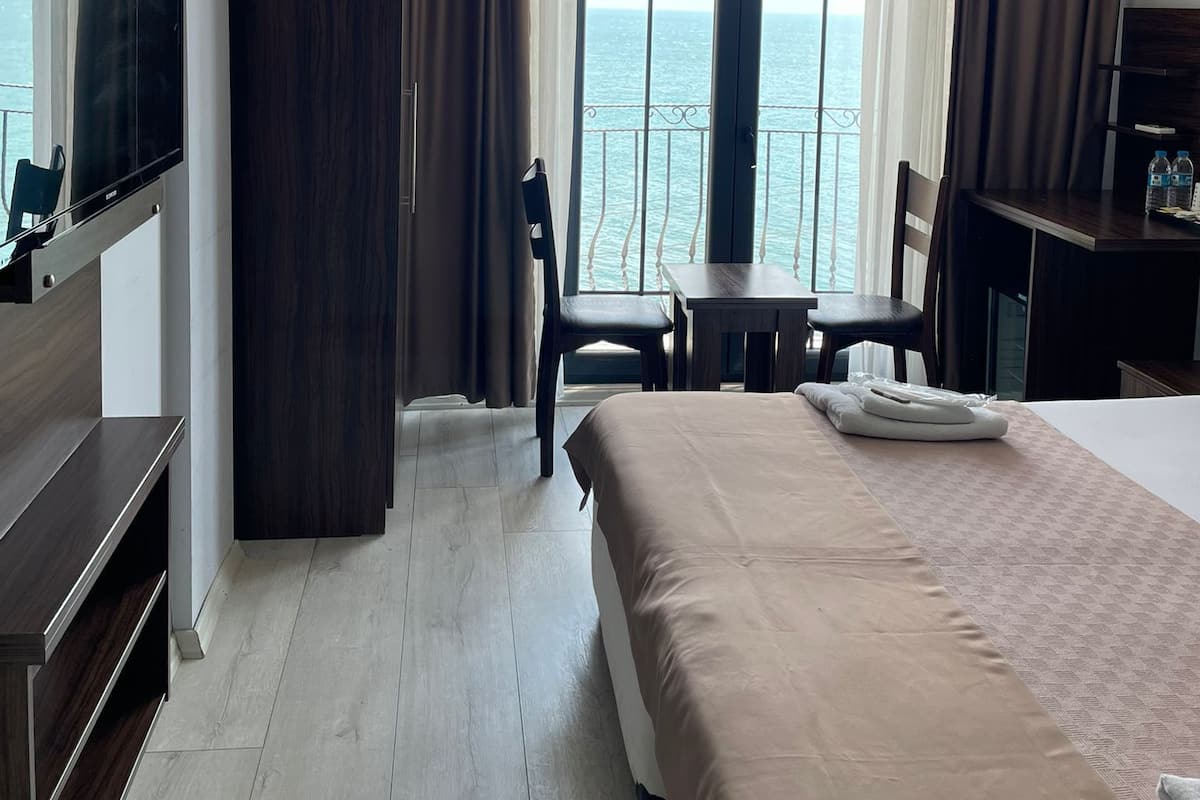 A hotel room with a bed, a TV, a desk, and a view of the sea.