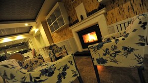 Ein gemütliches Wohnzimmer mit Kamin, floral gemusterten Sesseln und einer Ziegelwand.