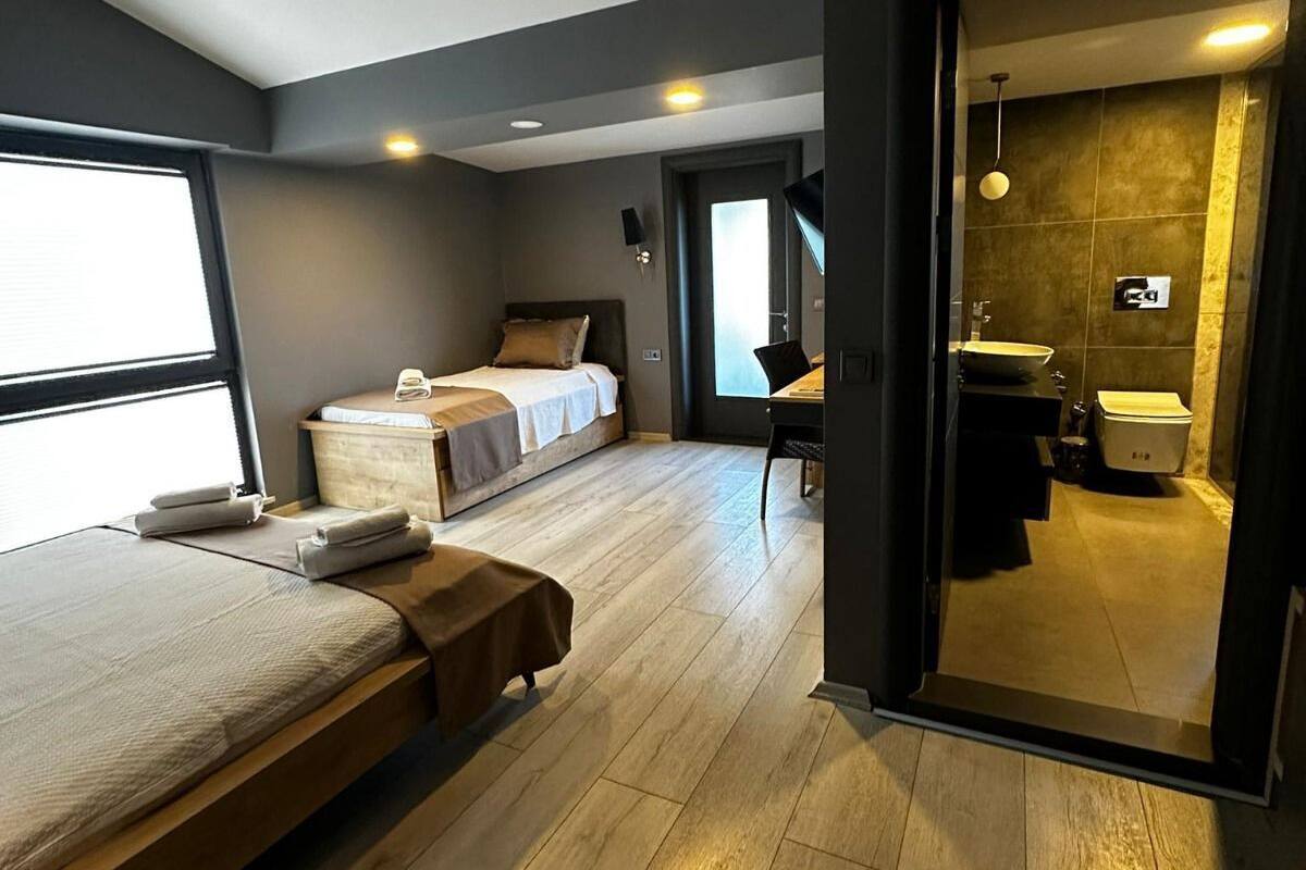 A modern hotel room with a large bed, a smaller bed, a desk, and a bathroom visible through an open door.