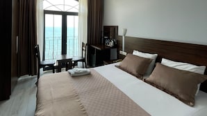 Ein Hotelzimmer mit einem großen Bett, einem Schreibtisch, einem Sessel und Blick auf das Meer.