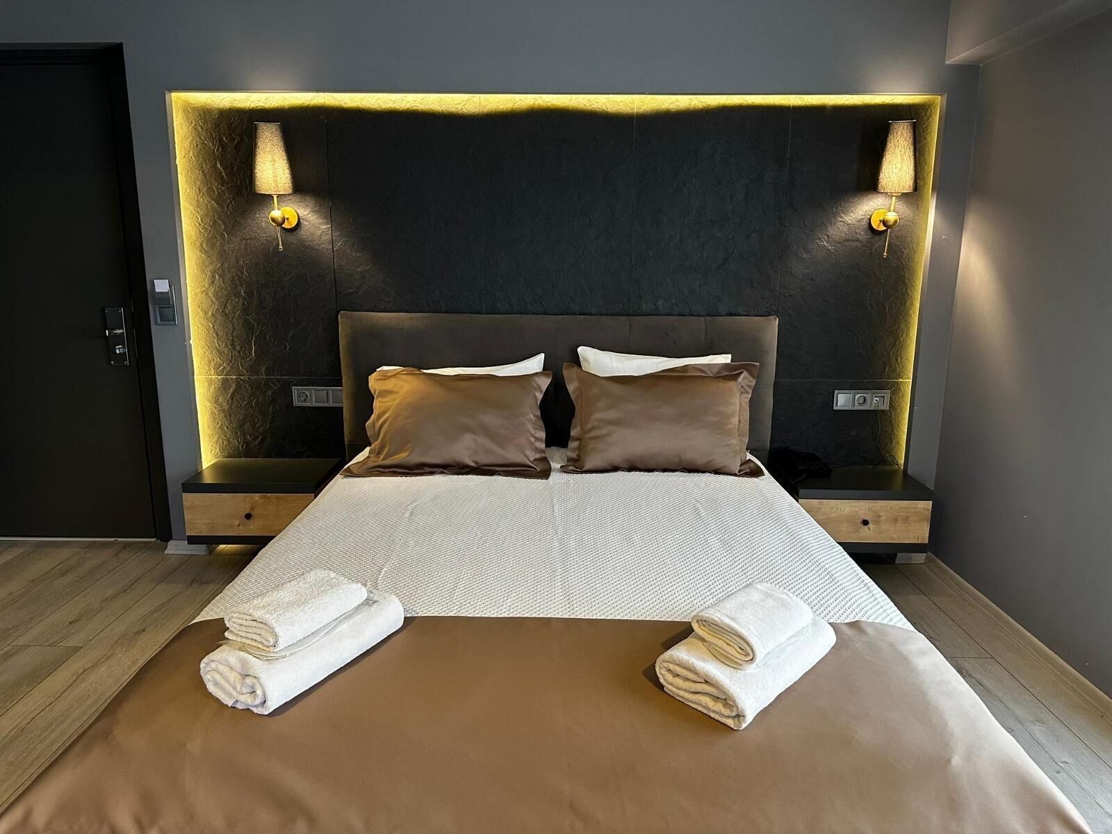 A modern hotel room with a large bed, two bedside tables, and wall-mounted lamps.