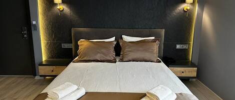A modern hotel room with a large bed, two bedside tables, and wall-mounted lamps.