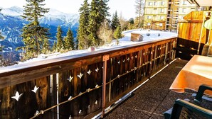 Een houten balkon met uitzicht op besneeuwde bergen en dennenbomen.