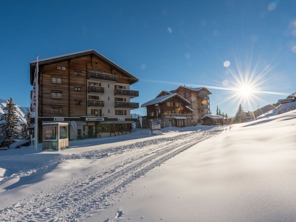 Et skiområde med træhuse, en klar himmel og en snedækket piste i sollys.