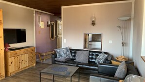 Een moderne woonkamer met een leren bank, houten kasten, een flatscreen televisie en een grote spiegel.