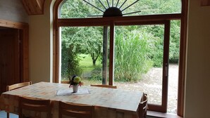 A dining area with a table and chairs, a potted plant, and a large arched window with a view of greenery outside. - Spacious holiday apartment in a thatched country house - including underfloor heating (Sydals)