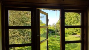 A room with a large open window revealing a well-maintained garden and trees. - Spacious holiday apartment in a thatched country house - including underfloor heating (Sydals)