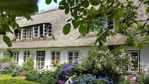 A traditional thatched-roof house with a well-maintained garden featuring a variety of flowers and shrubs. - Spacious holiday apartment in a thatched country house - including underfloor heating (Sydals)