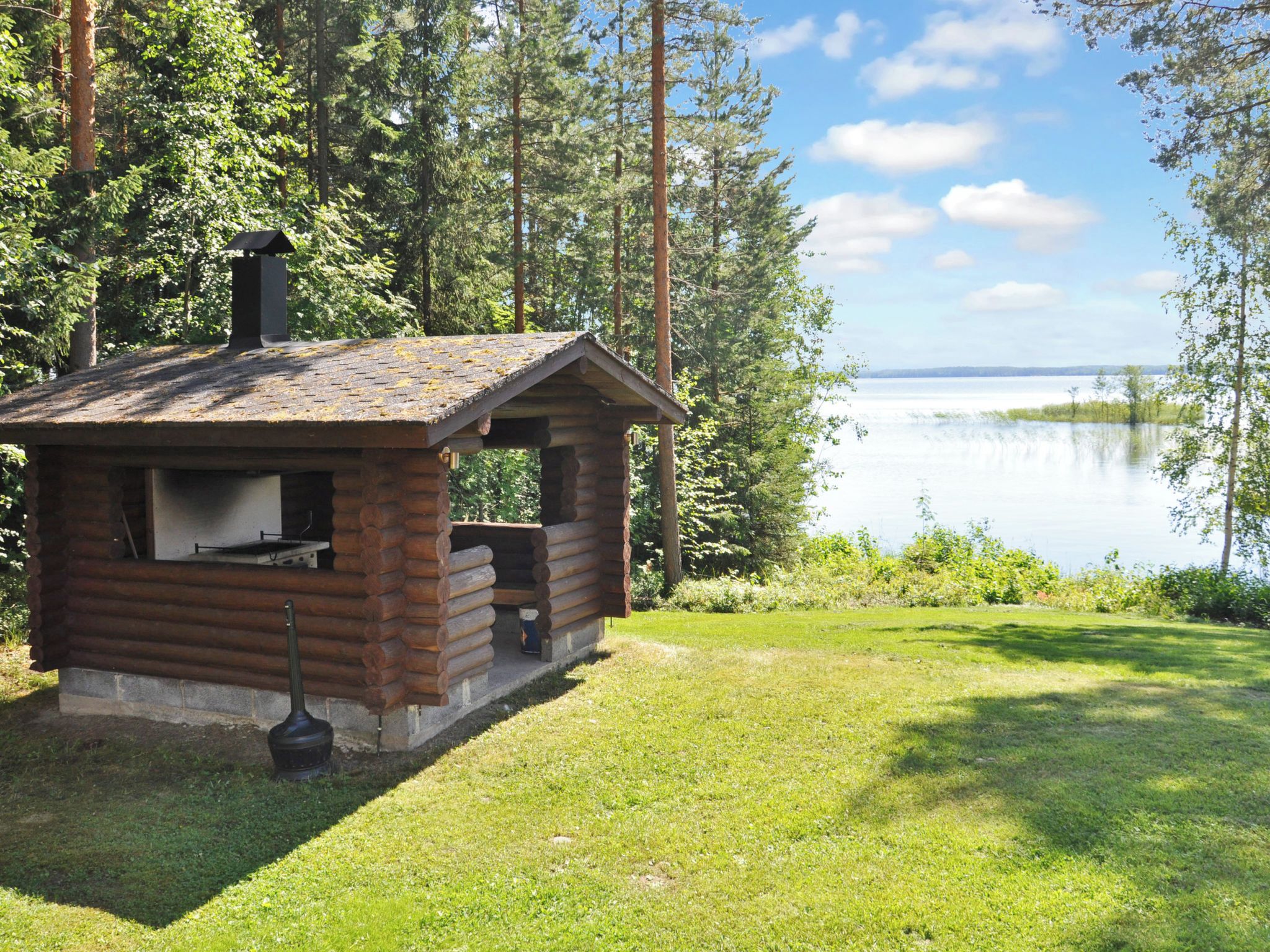 Une petite cabane en bois, dotée d’une cheminée, située près d’un lac entouré d’arbres.