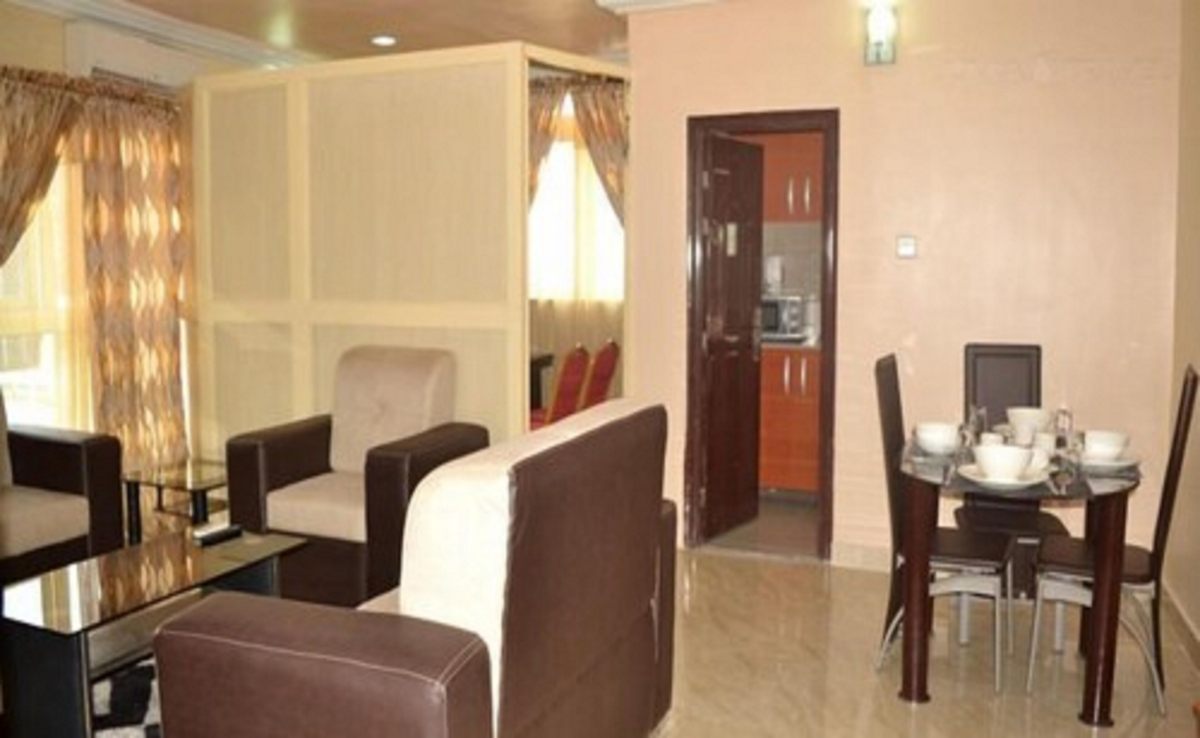 A hotel room with a dining area, a sofa, a TV, and a door leading to a kitchen.
