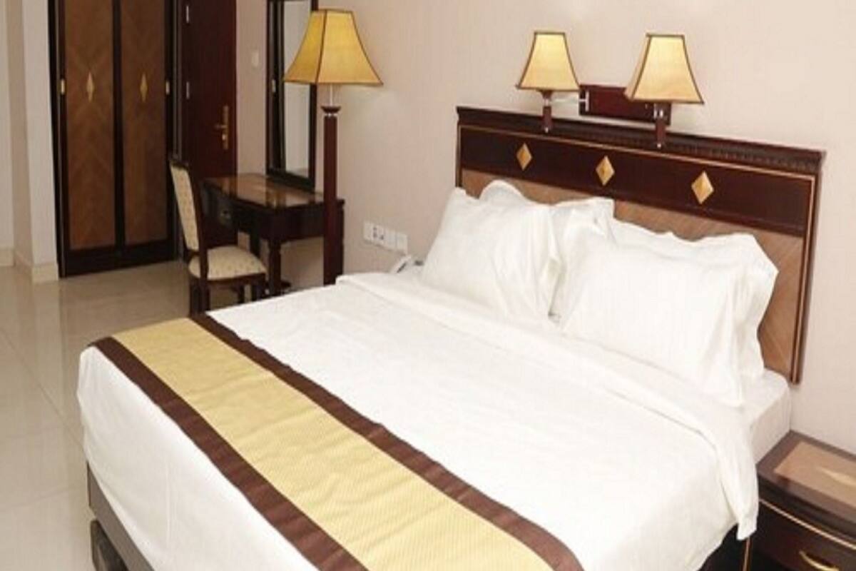 A hotel room with a large bed, two bedside lamps, a wooden headboard, a desk with a chair, and a mirror.