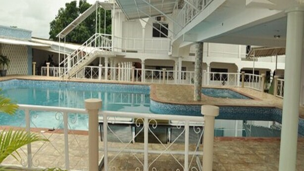 Un espace piscine doté d’une terrasse couverte, d’un escalier menant à un niveau supérieur et d’un sol carrelé.