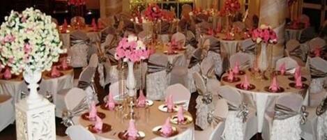 Un salón de banquetes con mesas redondas cubiertas con manteles blancos, cada una con centros de mesa rosas y sillas blancas.